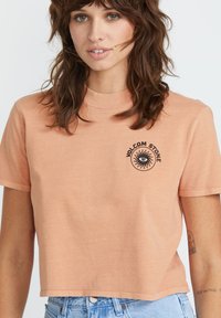 Różowa, krótka koszulka wykonana z miękkiego materiału, z czarną grafiką oka i napisem "Volcom Stone" z przodu. Krótkie rękawy i okrągły dekolt.