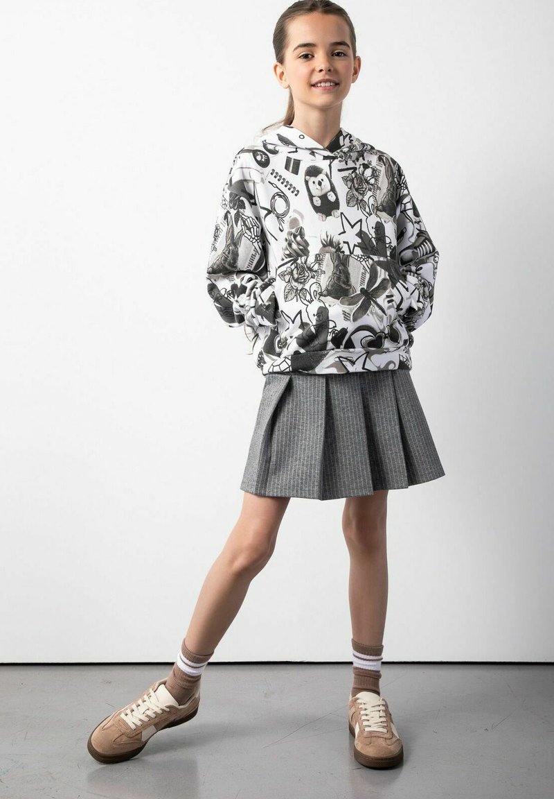 Bluza z kapturem z monochromatycznymi grafikami; szara spódnica plisowana; beżowe trampki z białymi akcentami; w komplecie z rajstopami w paski.