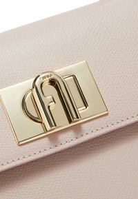 Borsa a tracolla in pelle rosa chiaro con texture, caratterizzata da una chiusura in metallo dorato con un logo distintivo e dettagli di cucitura visibili.