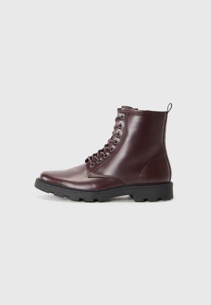 Botas de tobillo de cuero burdeos con acabado suave, punta redonda, suela de goma negra y ojales metálicos para los cordones. Tirador en el talón.