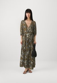 Maxi dress in olive green with white floral patterns, deep V-neck, puff sleeves, and tiered skirt; paired with a black textured handbag.
