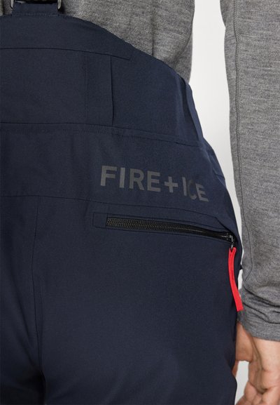 Marineblaue isolierte Hose mit einer Reißverschlusstasche mit rotem Reißverschluss und "FIRE+ICE"-Markierung. Das Material ist glatt und leicht.