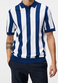 Námornický a bílý pruhovaný polo tričko, krátké rukávy, vyrobené z texturovaného pleteného materiálu. Má límec a patku na tři knoflíky, přiléhavý lem.