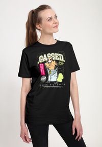 Černé bavlněné tričko s karikaturou a textem "Gassed! Fruity Tutty" v živých barvách, které zdůrazňuje hravou postavu.