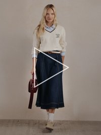 Krém színű, V-nyakú pulóver logóval, alatta világoskék ing, sötét farmer szoknya, fehér zokni, bézs tornacipő és bordó kézitáska.