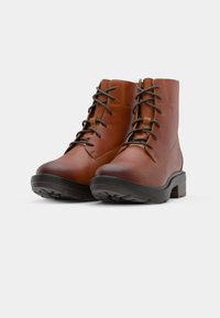 Botas de cuero marrón hasta el tobillo con punteras redondas, diseño de cordones y suelas de goma oscura en contraste. Detalles de costura sutil en los laterales.