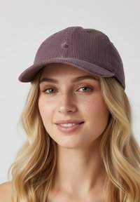 Casquette en velours côtelé violet avec une visière courbée et un logo brodé à l'avant. Présente une texture côtelée verticale et six œillets de ventilation.