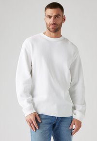 Hvit ribbestrikket genser med lange ermer, rund hals og teksturert stoff, kombinert med lyseblå slitte jeans.