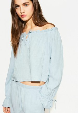 Light blue off-the-shoulder top with ruffled neckline, long sleeves, and a tied detail at the front. Made of soft, textured fabric.