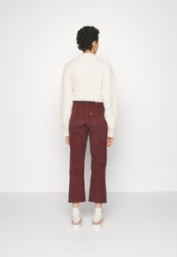 Pull en tricot crème avec un motif texturé, associé à un pantalon en velours côtelé bordeaux. La tenue est complétée par des chaussettes blanches et des baskets roses.