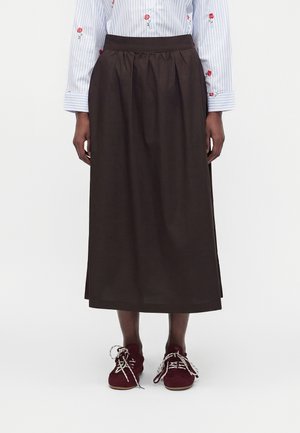 Longue jupe marron foncé portée avec une chemise légère rayée avec broderie florale rouge et des baskets bordeaux à lacets blancs.
