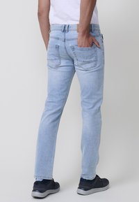 Jeans de denim azul claro con corte recto, que cuentan con dos bolsillos traseros y un ligero desgaste. Llevados con zapatillas oscuras.