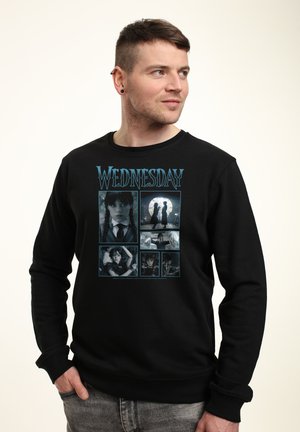 Mand iført sort sweatshirt med seks scener fra serien "Wednesday", herunder en pige med fletninger og gotiske visuelle elementer.