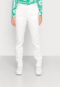 Calças brancas, leves, com um corte descontraído, apresentando uma textura suave e uma cintura padrão. Combinadas com ténis brancos e uma blusa com padrão verde.