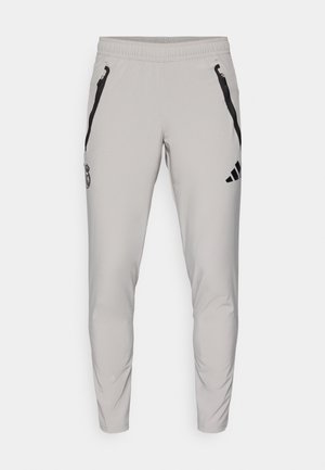 Calças atléticas cinza claro feitas de tecido suave, com bolsos com fecho éclair pretos e um logótipo bordado na coxa esquerda. Design de corte justo.