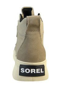 Beige suede ankle boot with a textured finish, white rubber sole, and a black "SOREL" logo on the heel. Features a pull tab at the back.