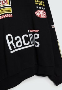Sudadera negra con parches bordados en blanco y de colores que presentan texto con temática de carreras, patrones a cuadritos y varios acentos de logotipos.