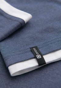 Námořnická modrá bavlněná tričko s bílými akcenty kolem límce. Obsahuje malou černou etiketu se slovem "ombre" poblíž lemu.