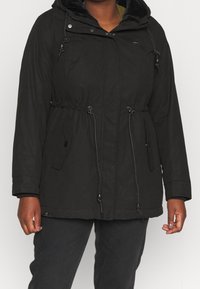 Parka noire avec capuche, taille élastique, poches zippées et doublure intérieure douce. Tissu texturé avec une finition extérieure lisse.