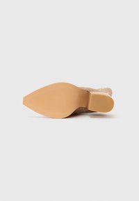Semelle d'une botte chelsea beige à bout pointu avec un talon carré, présentée sur un fond blanc uni.