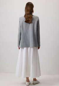 Pilkas šydelis su dryžiais, laisvas kirpimas, derinamas su balta, pūkuota maksi sijonu. Balti batai užbaigia aprangą. Fonas neutralus.