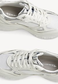 Bílé sportovní tenisky vyrobené ze síťoviny a syntetických materiálů, s tkaničkami, texturovaným povrchem a mírně vyvýšenou podešví.