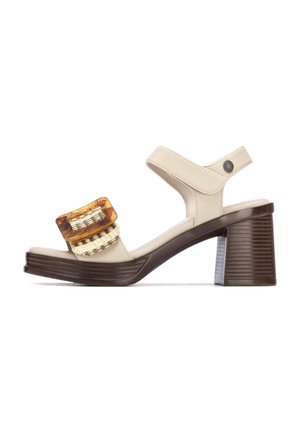 Sandalia beige con un tacón grueso y cuadrado de color marrón, que cuenta con una hebilla decorativa de tono ámbar y un detalle tejido dorado en la correa superior.