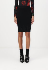 Jupe noire côtelée en tricot avec une coupe ajustée, présentant une finition texturée et une lueur progressive vers l'ourlet. Accentuée par des chaussures à bouts pointus.