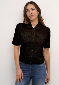 Svart denim skjorta med korta ärmar, krage, knäppning framtill, två bröstfickor och en figurnära passform. Slät textur.