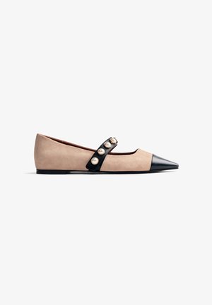 Shoe plano bege com bico preto pontiagudo, tiras pretas adornadas com grandes pérolas na parte superior e sola preta baixa.