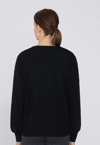 Schwarzer Strickpullover mit rundem Halsausschnitt und langen, leicht puffigen Ärmeln. Der Rücken ist schlicht mit gerippten Manschetten und Saum.