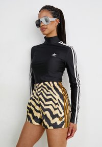 Μαύρη μπλούζα με μακριά μανίκια και λευκές ρίγες, συνοδευόμενη από σορτσάκι με σχέδιο ζέβρας σε κίτρινο και μαύρο που διαθέτει κατακόρυφες ρίγες.