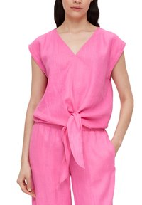 Roze, lichtgewicht linnen top met een V-hals en korte mouwen, voorzien van een voorste strikdetail. Bijpassende losvallende roze broek zichtbaar.