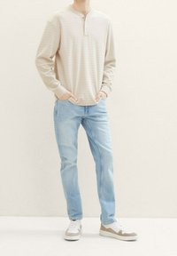 Beige gestreiftes Langarm-Henley-Hemd, blaue Jeans und mehrfarbige Turnschuhe; lässige Passform mit gerippten Bündchen und geknöpftem Ausschnitt.
