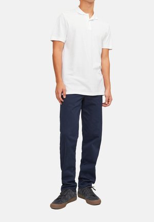 Hvid kortærmet polo skjorte, marineblå bukser og sorte sneakers med brune såler. Outfittet har et klassisk snit og en afslappet design.