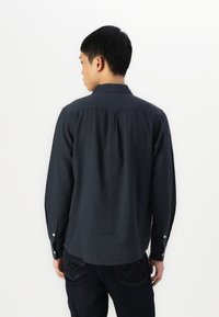 Camicia a maniche lunghe blu scuro con colletto, dotata di spalline dritte e bottoni ai polsini. Tessuto testurizzato con dettagli minimi.