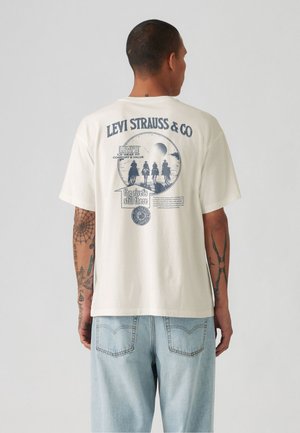 T-shirt in cotone color crema con grafica stampata sul retro che presenta un design circolare, testo e silhouette di cavalieri. Vestibilità rilassata, maniche corte.