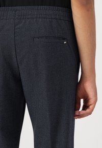 Pantalones texturizados en color azul marino con un bolsillo trasero que tiene un pequeño detalle metálico. Cintura elástica, corte entallado y un patrón de tejido sutil.