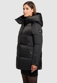 Geacă puff neagră cu guler înalt, buzunare cu fermoar și design căptușit. Are un material lucios, neted și un patch cu logo pe mânecă.