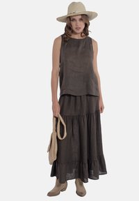 Linnen twee-delig outfit met een mouwloze top en een gelaagde rok in donkerbruin, gecombineerd met beige laarzen en een strohoed. Inclusief een geweven tas.