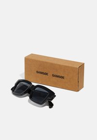 Black square sunglasses with thick frames and dark lenses, displayed in a brown cardboard box labeled "SAMSOE."