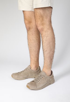 Beige suede sneakers with a rounded toe, minimal lacing, and a textured design. The sole is light brown with a rubber finish.