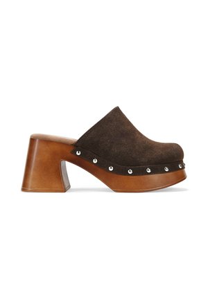 Zueco de ante marrón con un tacón de madera grueso. Presenta tachuelas metálicas a lo largo de la base y una textura suave. Diseño elegante y redondeado.