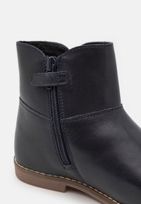 Kožené kotníkové boty v námořnické modři se zipovým uzávěrem, polstrovaným interiérem a texturovaným povrchem. Vybaveny hnědou gumovou podrážkou a prošitými detaily.