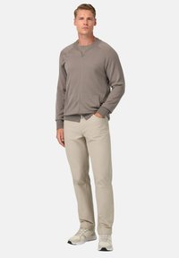 Chaqueta gris con cremallera frontal y puños acanalados, combinada con pantalones beige claros y zapatillas blancas. Diseño simple con un corte relajado.