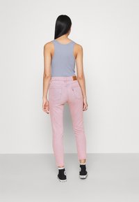 Vaqueros de mezclilla rosa con un diseño ajustado y estilo de cinco bolsillos, combinados con una blusa sin mangas de color azul claro. Zapatillas de lona negras de caña alta visibles.
