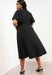 Rochie neagră cu mâneci scurte evazate, tiv pe genunchi și corset ajustat. Material neted și detalii discrete ale cusăturilor la spate.