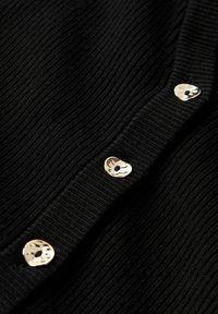 Svart ribbat cardigan med tre metalliska bladformade knappar längs öppningen, som visar ett texturerat stickmönster.