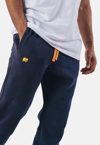 Námořnické tepláky s oranžovou šňůrkou, na stehně s malým žlutým logem slona, vyrobené z měkkého materiálu s hladkou texturou.