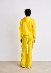 Felpa gialla con cappuccio dal design corto abbinata a pantaloni cargo coordinati, dotati di tasche laterali e vestibilità ampia.